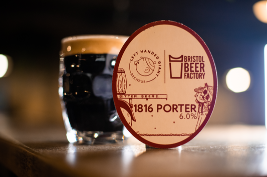 A dimpled pint glass of dark porter with cream head sat next to an 1816 Porter pumpclip